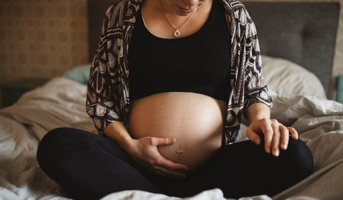 En gravid kvinna sitter på en säng.