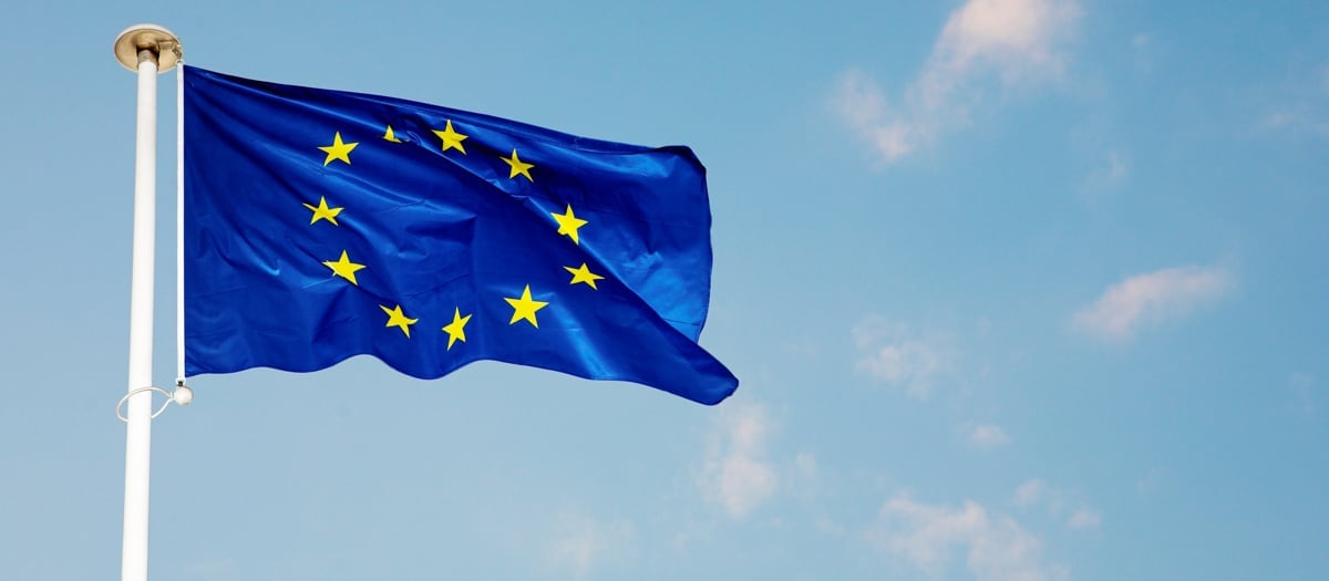 Bild på en blå EU-flagga som vajrar på en vit flaggstång med blå himmel i bakgrunden