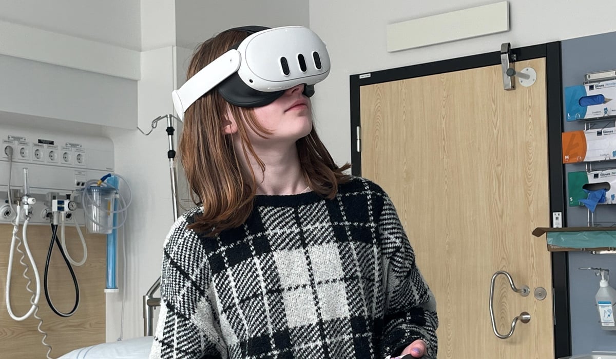 En flicka i 10-årsåldern står med VR-headset och handkontroller i ett sjukhusrum