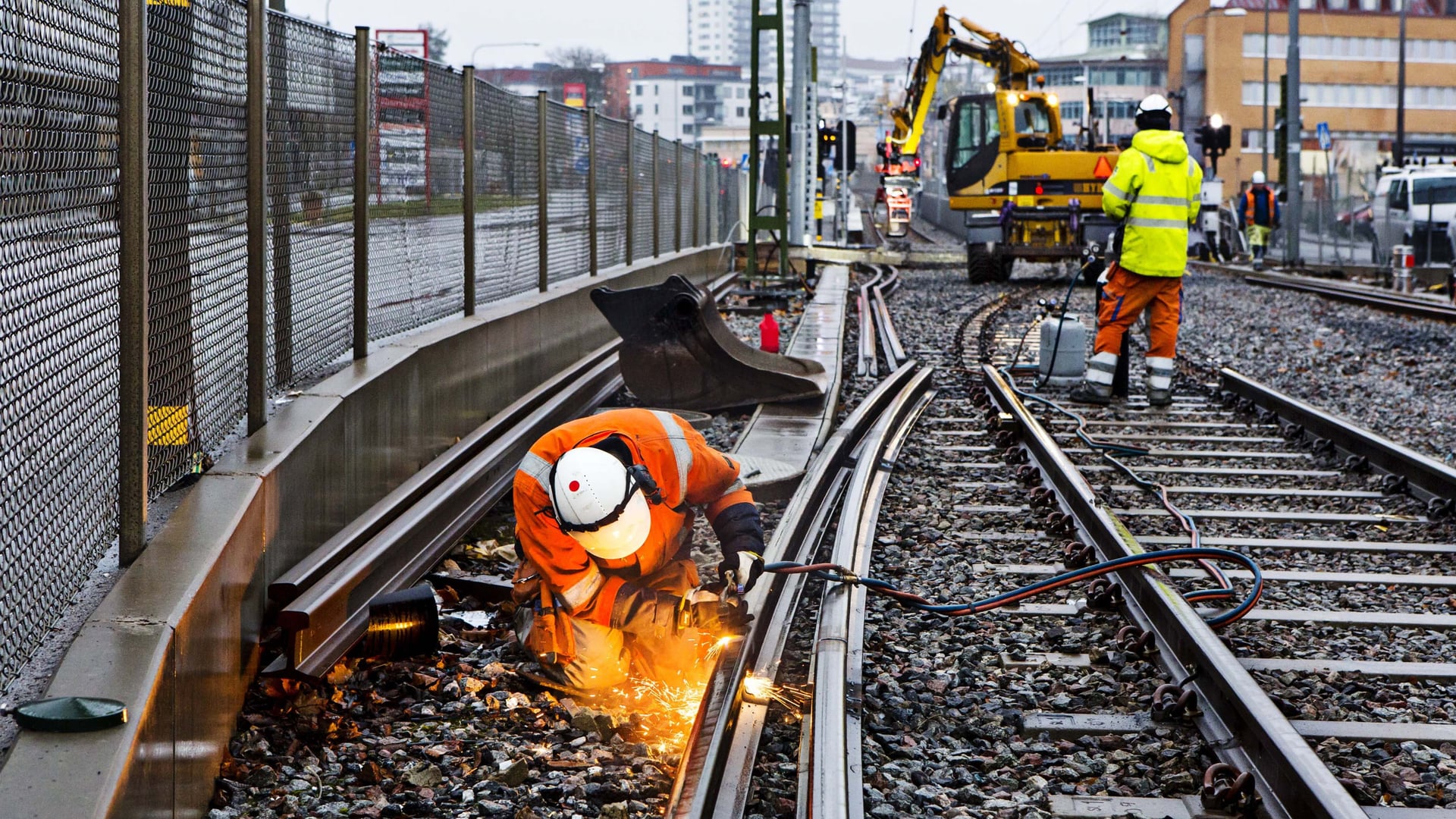 Två män i orange arbetar på ett tågspår.