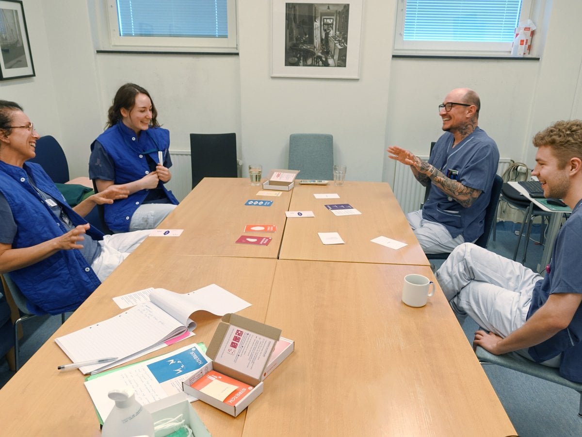 Foto på flera personer som sitter runt ett bord. De är klädda i sjukhuskläder.