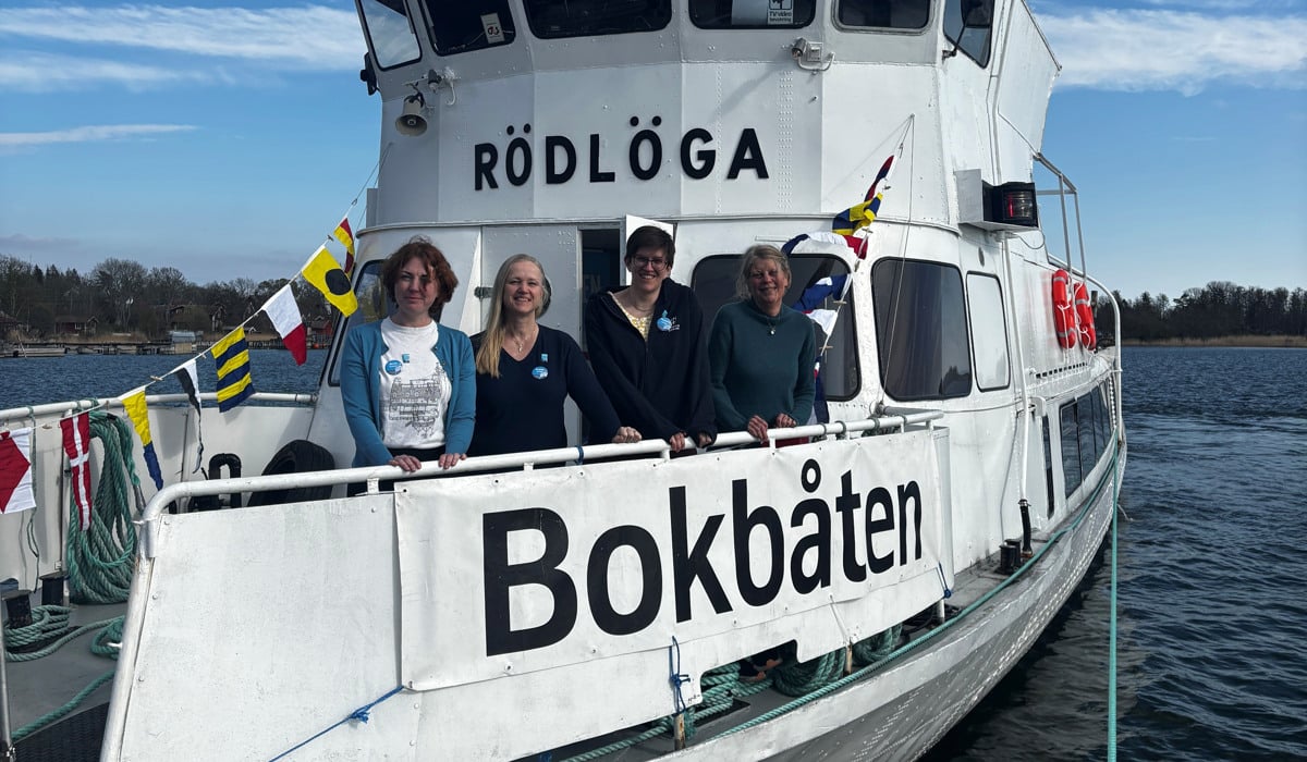 En grupp människor på en båt i vattnet. Båten har en dekal med namnet bokbåten.