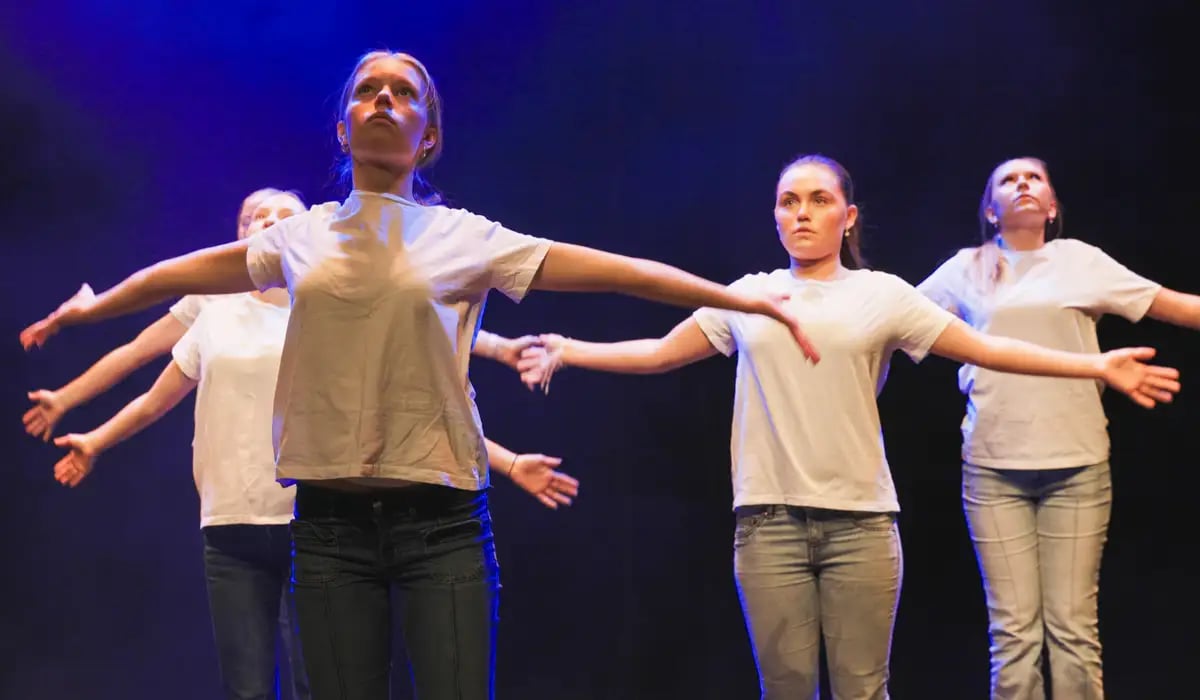 Fyra unga kvinnor i vita t-shirts och jeans dansar med utsträckta armar.