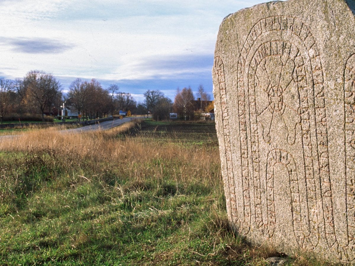 Landskap med en runsten i förgrunden. 