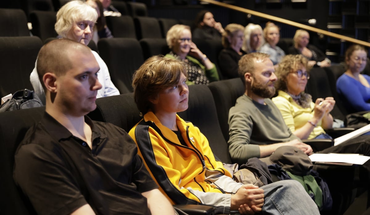 Människor som sitter i en upplyst biografsalong och lyssnar på en presentation