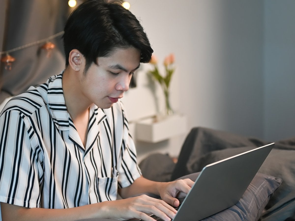 En pojke med svartvitrandig skjorta sitter i en soffa och skriver på en dator.