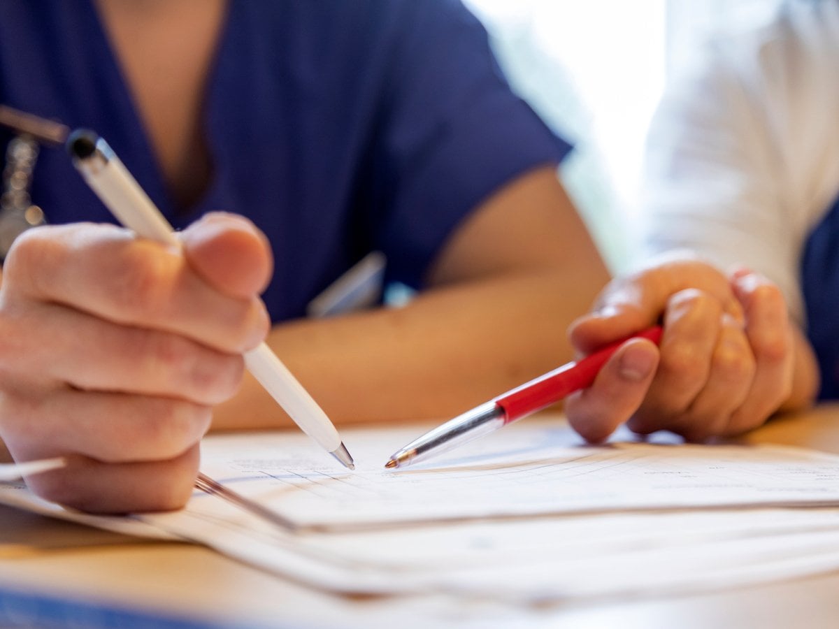 Närbild på två personer som håller i en penna och pekar på ett papper