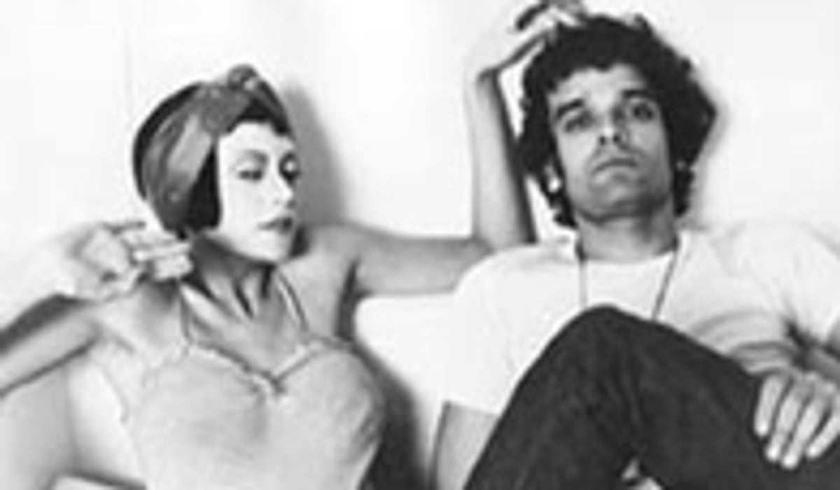 Filmruta med en kvinna och en man som halvligger i en soffa. Kvinnan är väldigt sminkad och mannen ser uttråkad ut. Bilden är svart-vit.