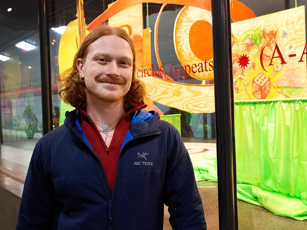 Stolt Nils framför glasmontern. Här står en text på en enda lång rad i ögonhöjd runt montern. Tygstycken och utskurna symboler i träpaneler fyller montern.