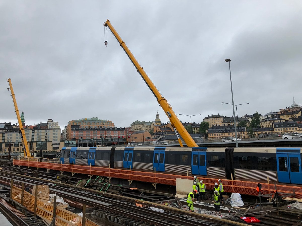 Tunnelbanetåg modell C20 åker över Söderströmsbron. I bakgrunden syns lyftkranar och människor som arbetar på spåret.