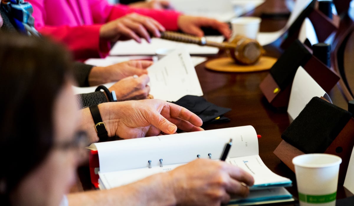 Inzoomad bilder som fokuserar på händer tillhörande mötesdeltagare runt ett mötesbord. 