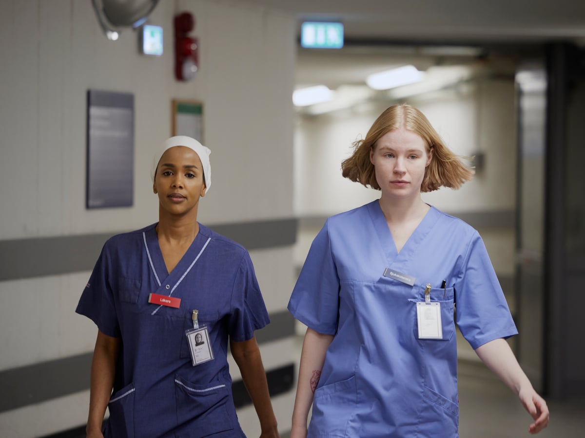 Två kvinnor i operationskläder går längs en korridor.