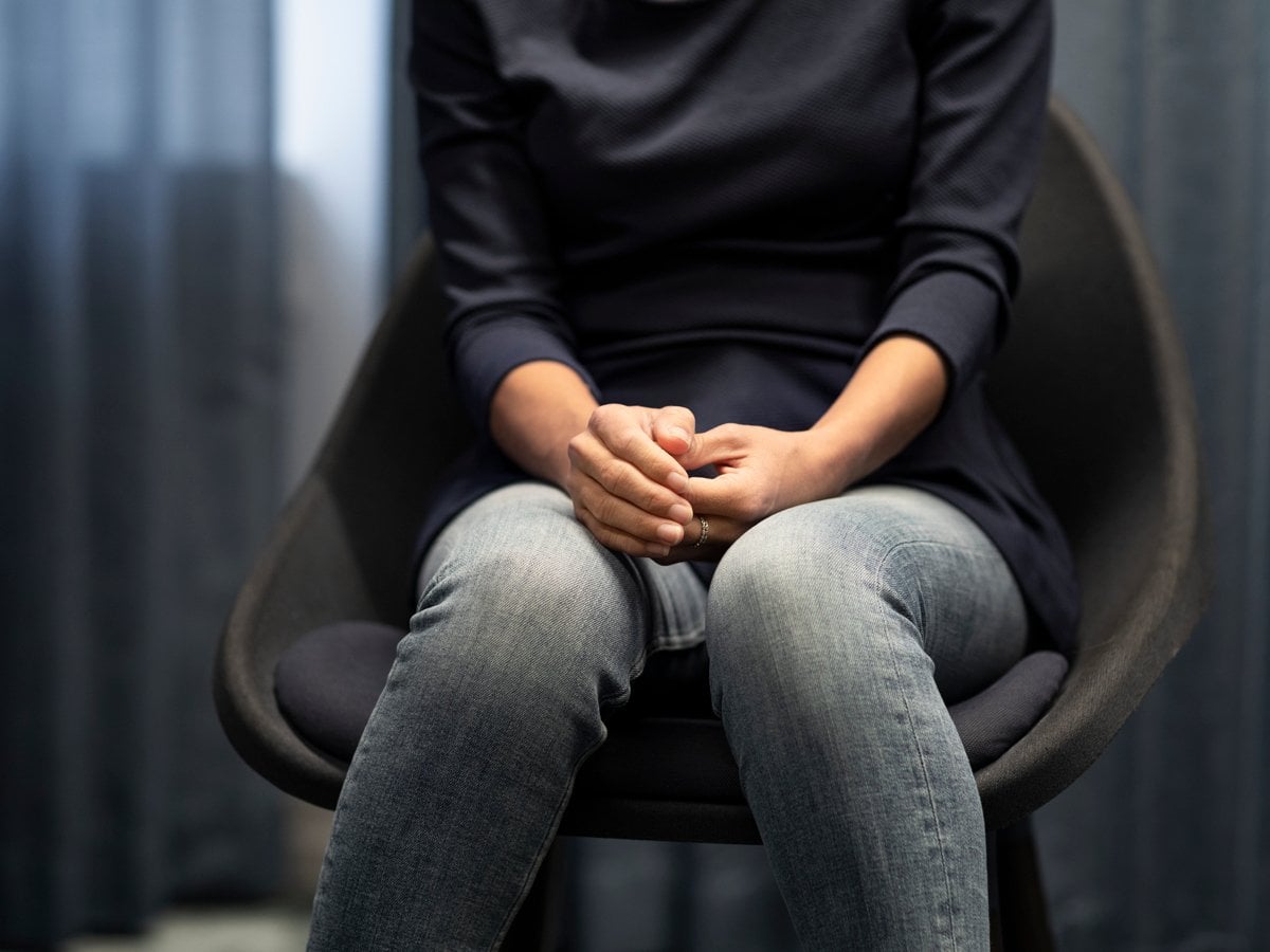 Kvinna sitter i stol med händer i knät. Huvudet är utanför bild.