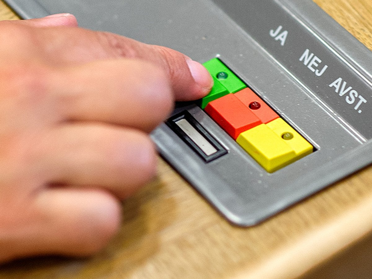 Hand som håller finger på Ja-knappen i landstingssalen.