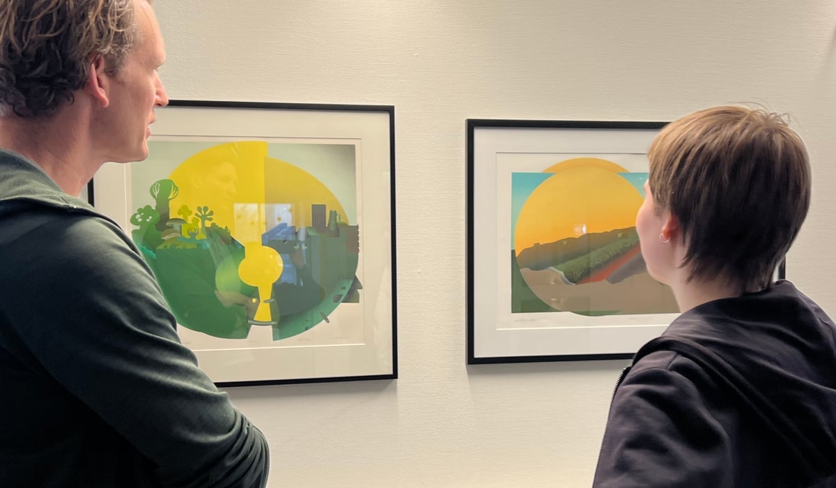 Två personer står och tittar på två tavlor på en vägg.