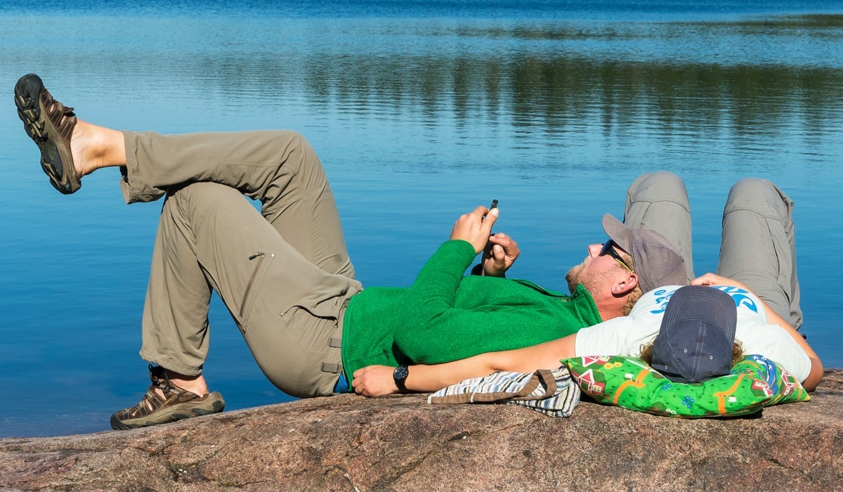 Två personer ligger på en klipphäll framför vatten.