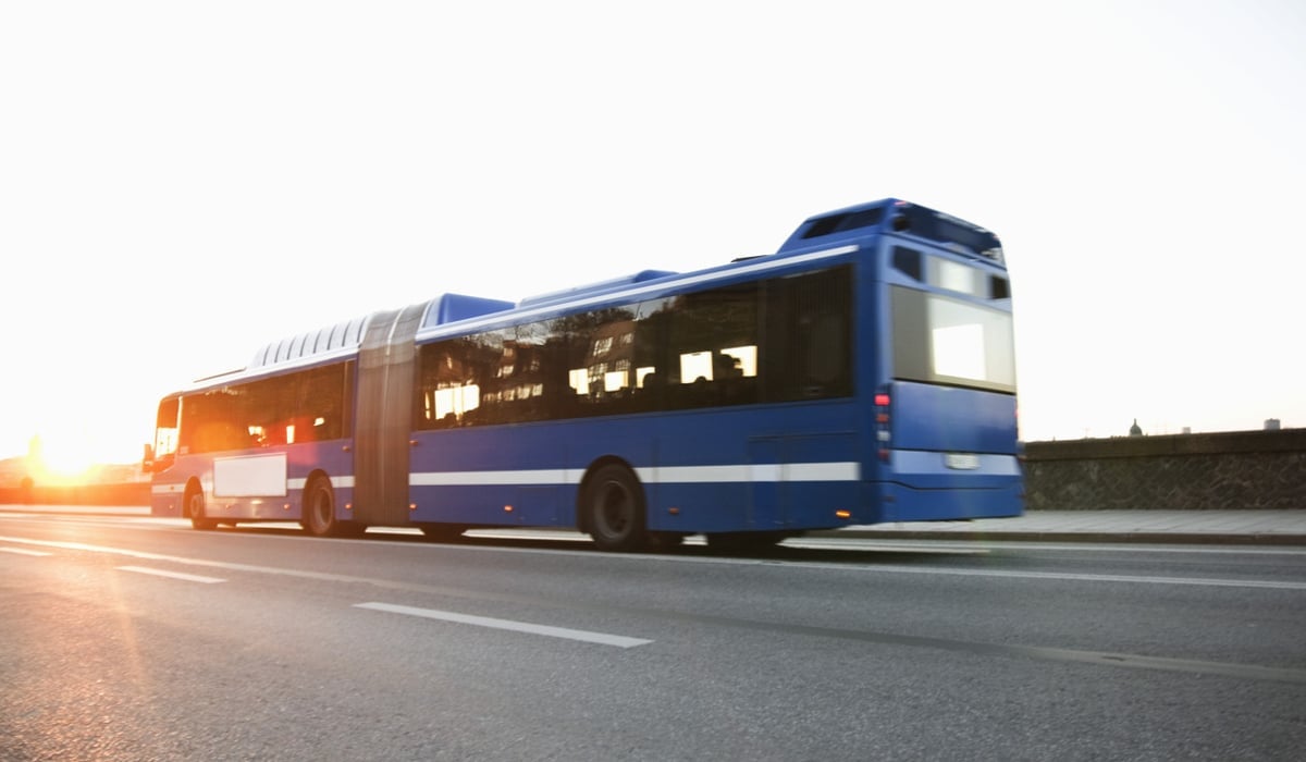 En blå buss kör längs en gata bredvid en annan buss.
