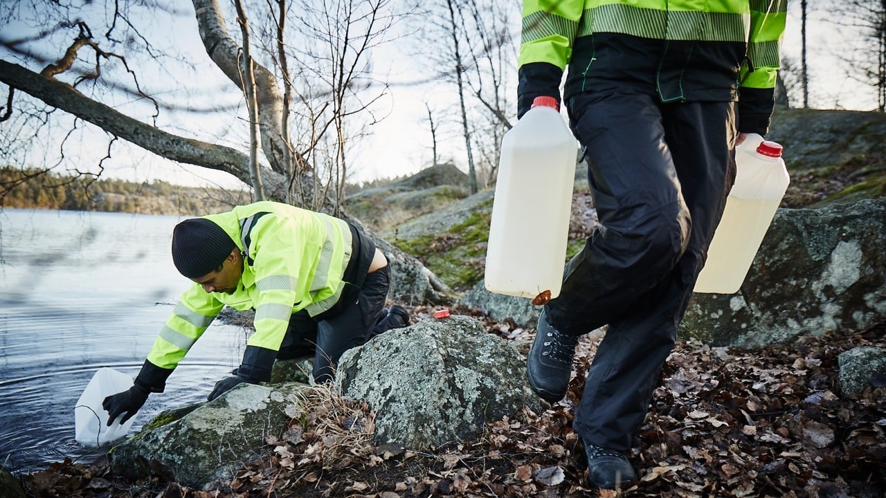Två personer i varselvästar hämtar vatten ur en sjö