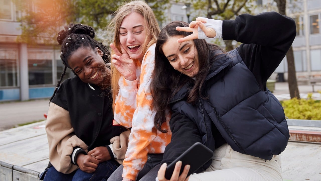 Tre tjejer i tonåren tar en selfie på sig tillsammans, utomhus