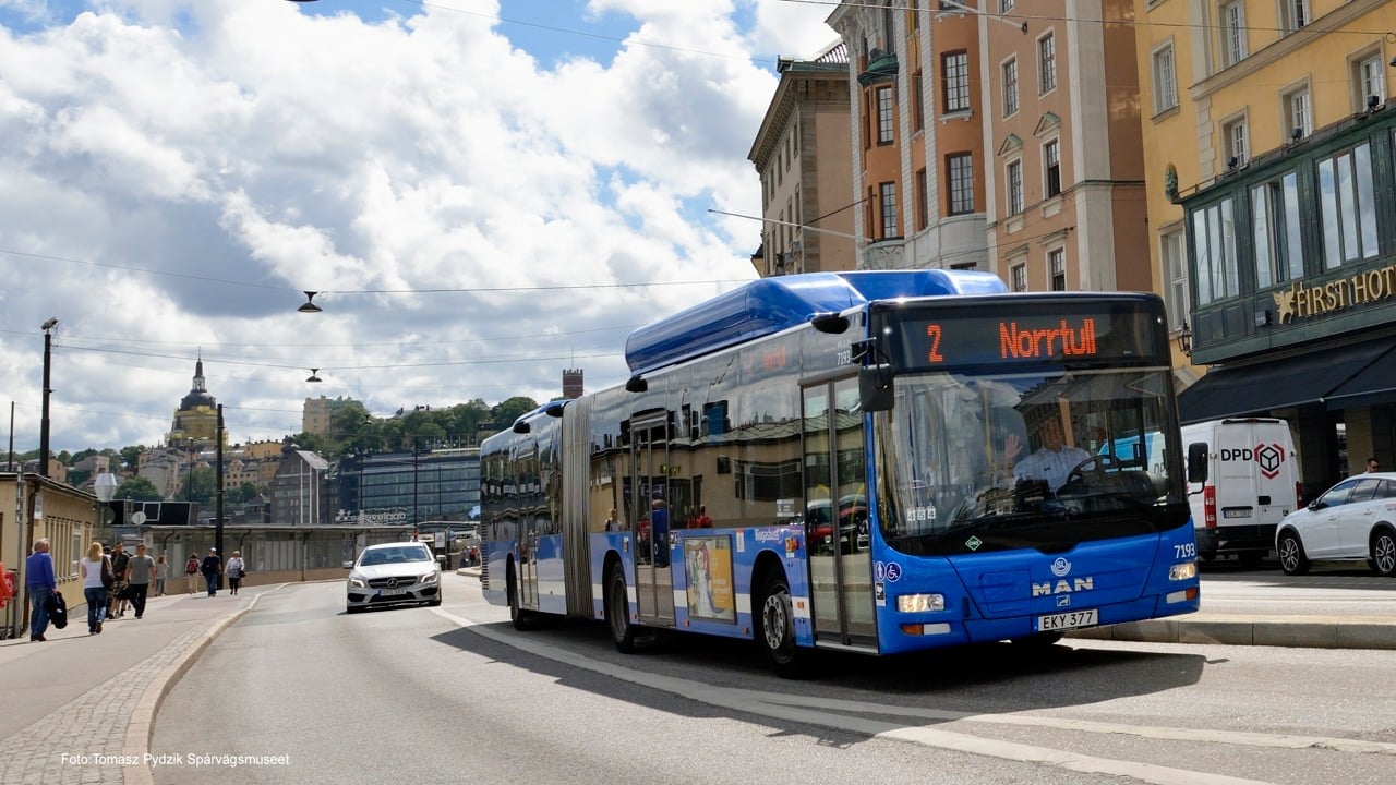 En blå stadsbuss åker förbi skeppsbron i ett soligt Stockholm