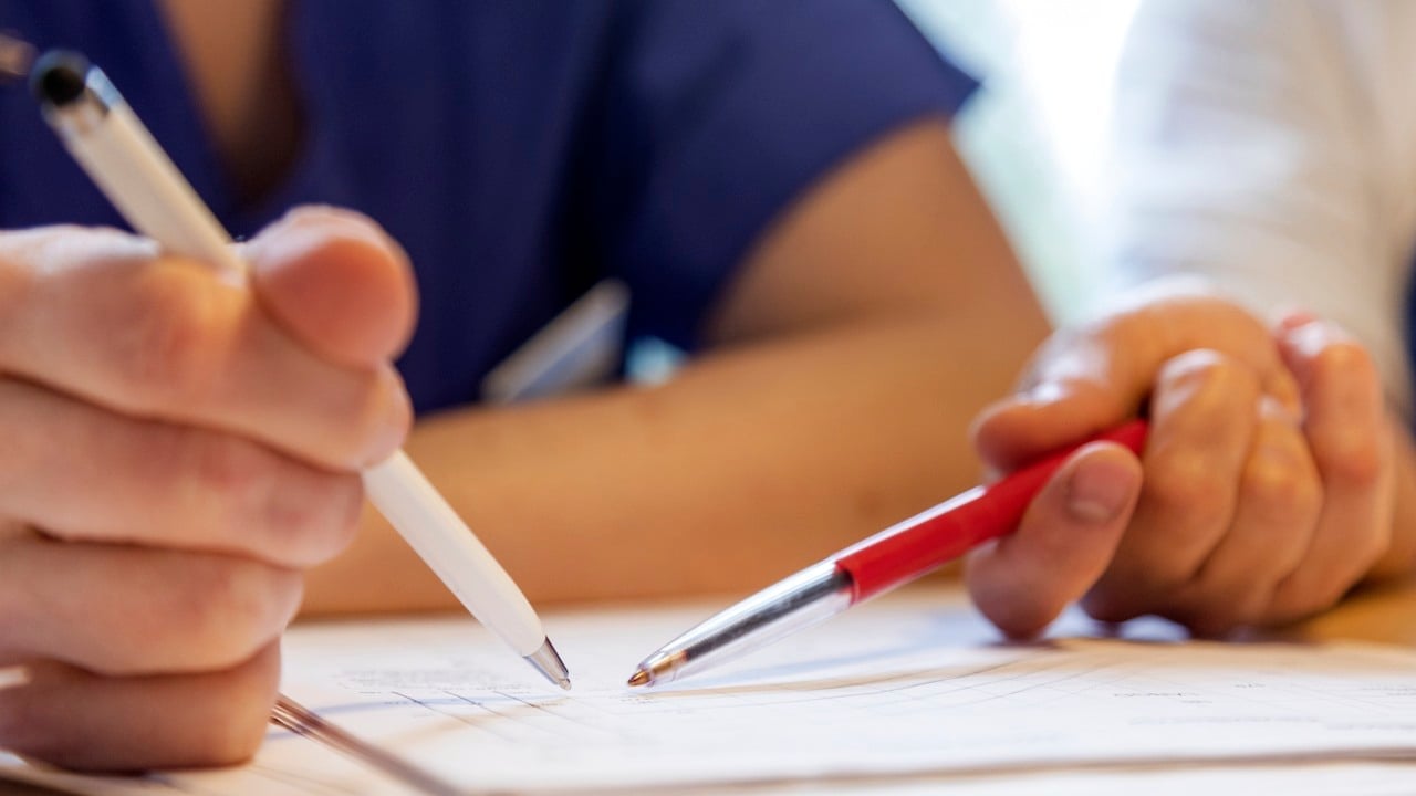 Två händer som håller i varsin penna som de pekar med på ett dokument