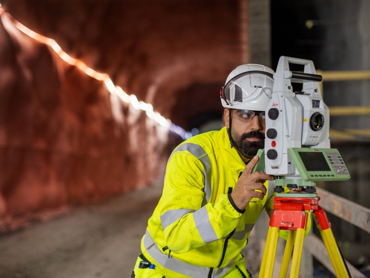 Man i arbetskläder och som tittar intensivt in i ett mätinstrument som står på stativ inne i en tunnel