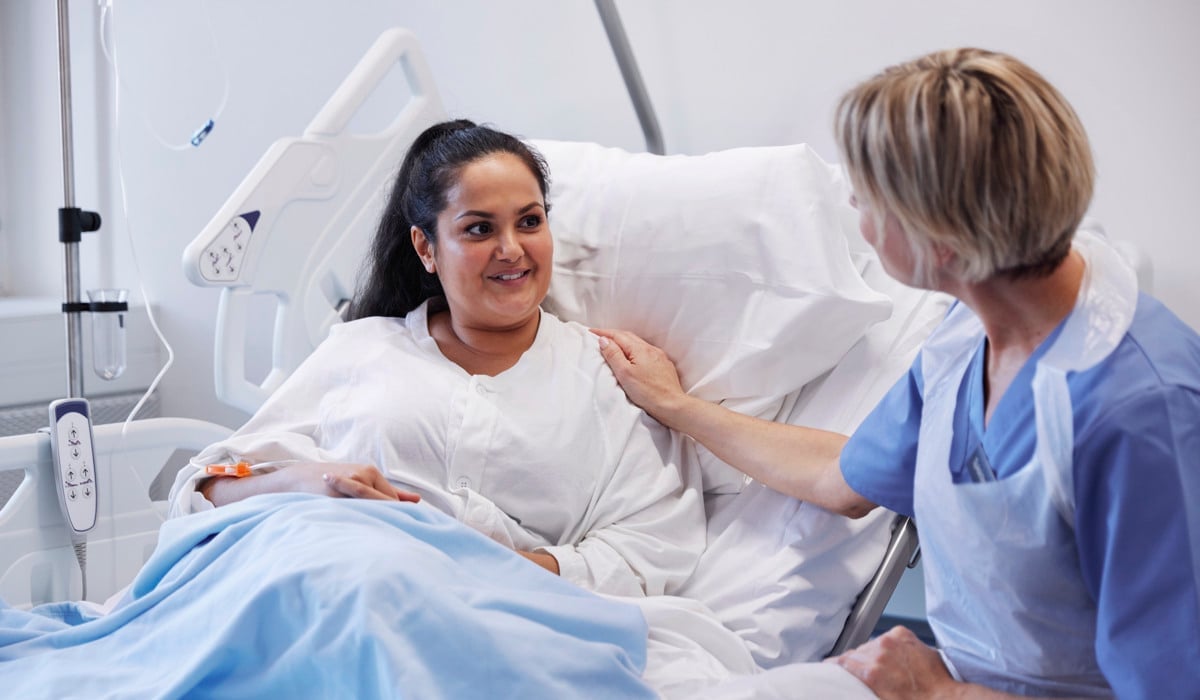 En patient sitter i en sjukhussäng och pratar med en sjukvårdspersonal