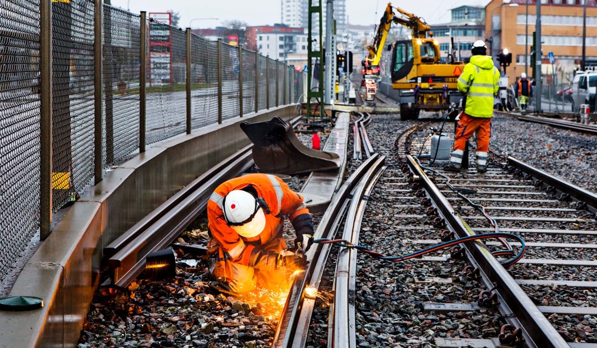 Två män i orange arbetar på ett tågspår.