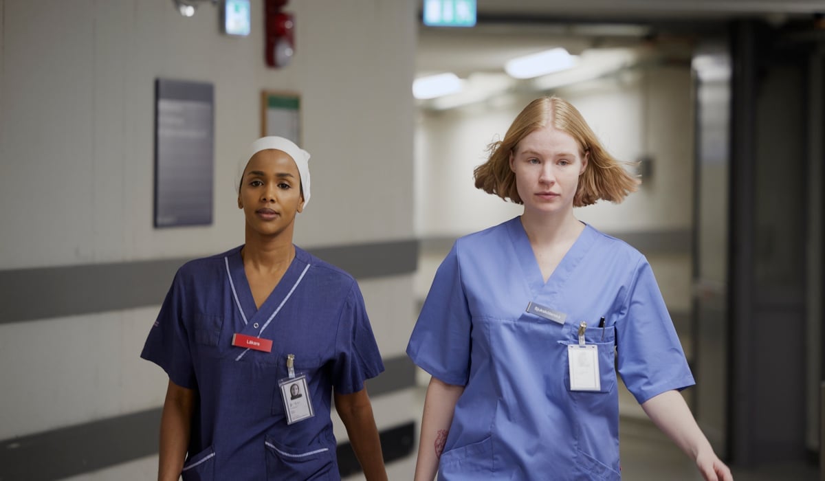 Två kvinnor i operationskläder går längs en korridor.