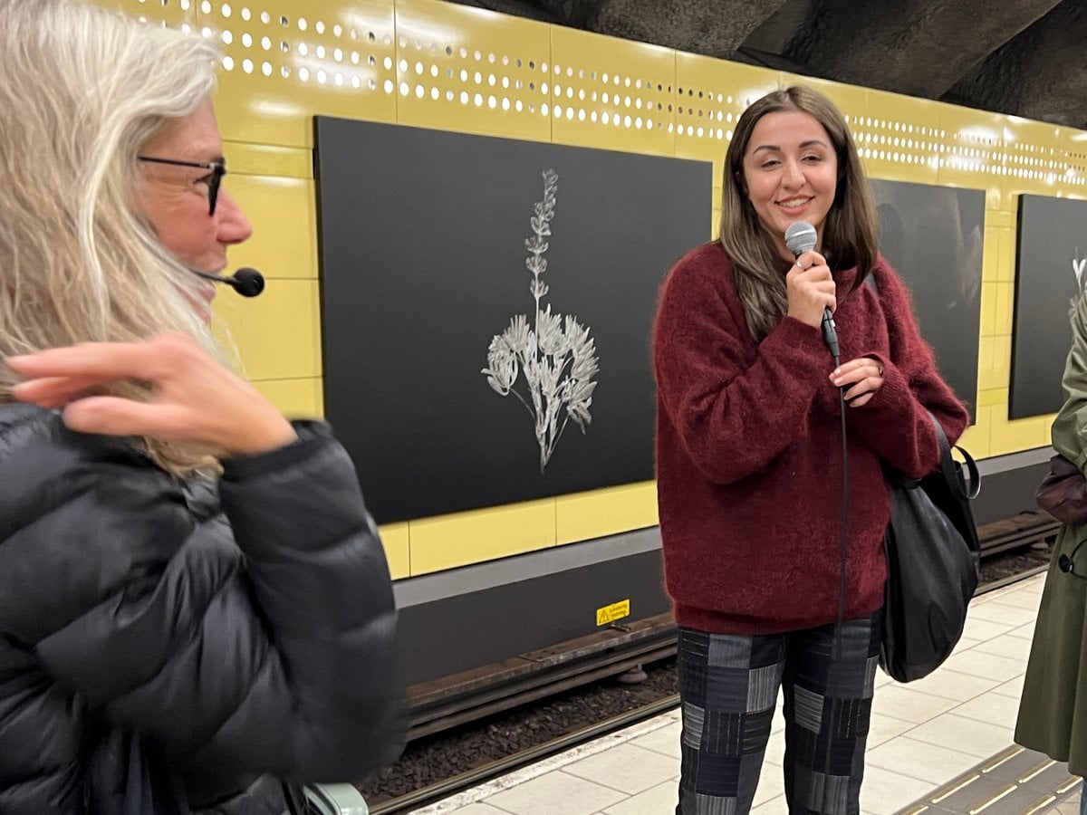 Jasmin pratar i mikrofon sida vid sida med en konstguide framför fotografierna på Fridhemsplan.