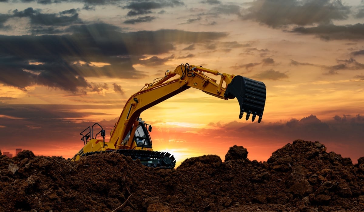 En gul grävskopa arbetar i skymningen.