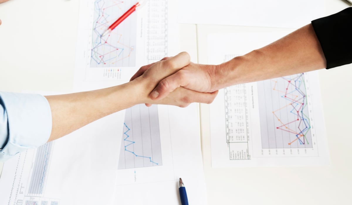 Två händer som skakar hand över ett bord med papper