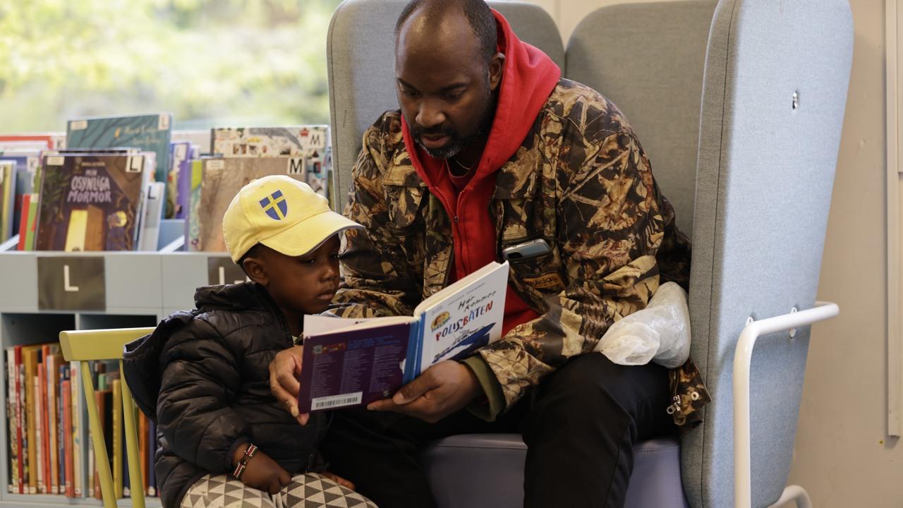 Pappa och son som läser en bok på biblioteket