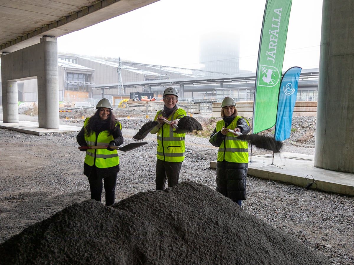 Tre personer iklädda varselväst och hjälm står vid en hög grus och tar ett varsitt symboliskt första spadtag.