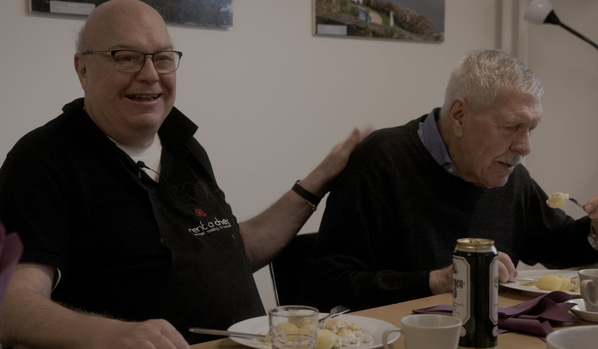 Två äldre män sitter vid ett bord och äter mat.