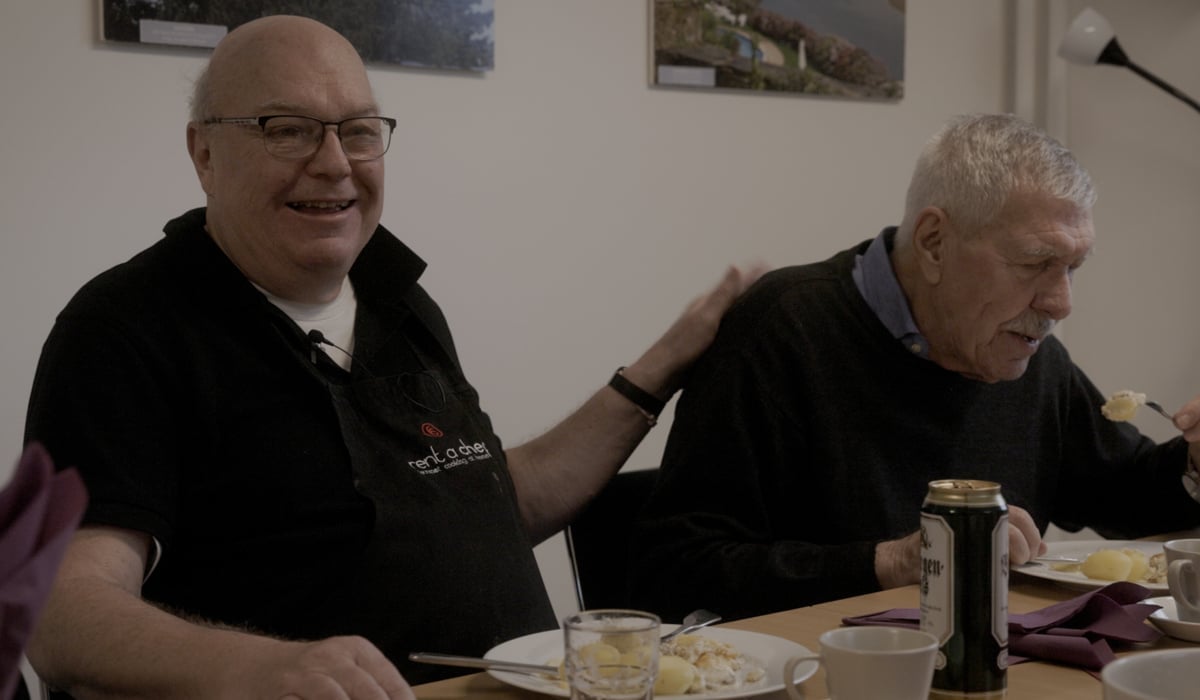 Två äldre män sitter vid ett bord och äter mat.