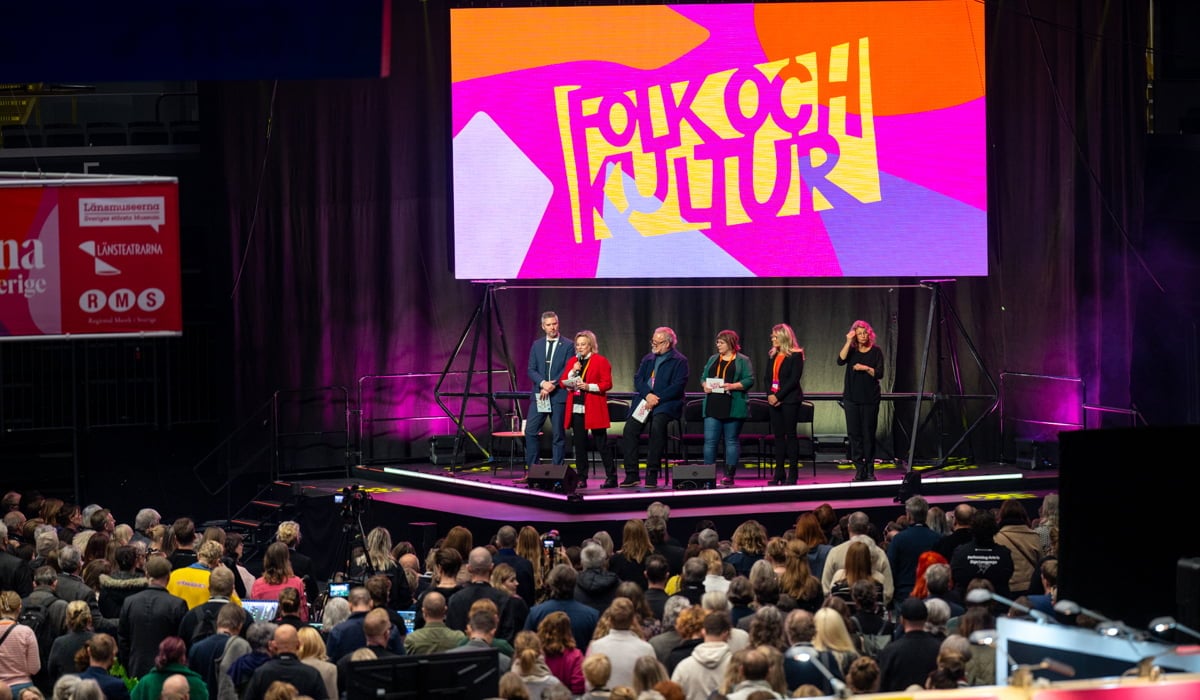 Ett publikhav framför en scen med en panel och en skärm där det står Folk och kultur