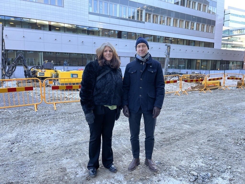 En man och en kvinna står framför en byggnad vid en byggarbetsplats.