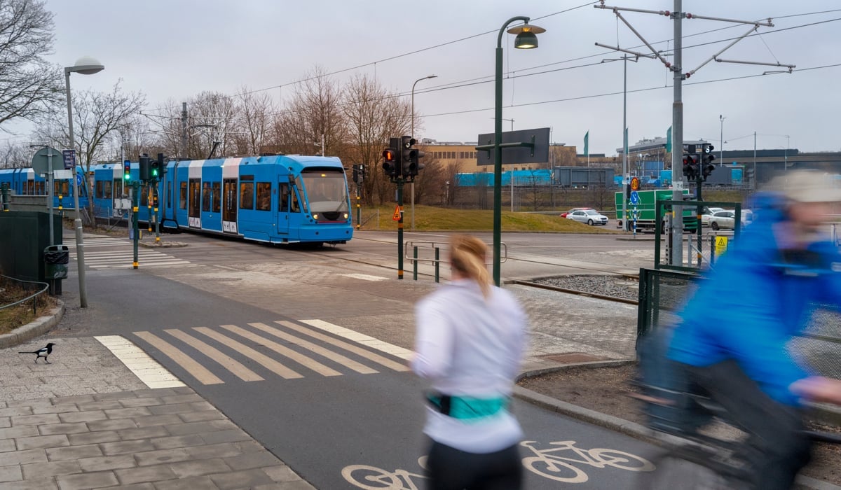 En man cyklar längs en gata bredvid en blå buss.