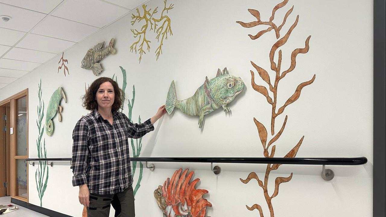 Ida håller handen mot väggen med målade växter och fantasitdjur.