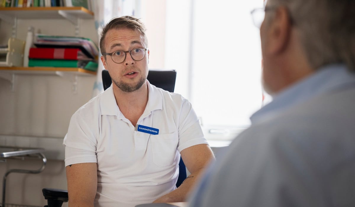 En man sitter i en stol och pratar med en annan man.