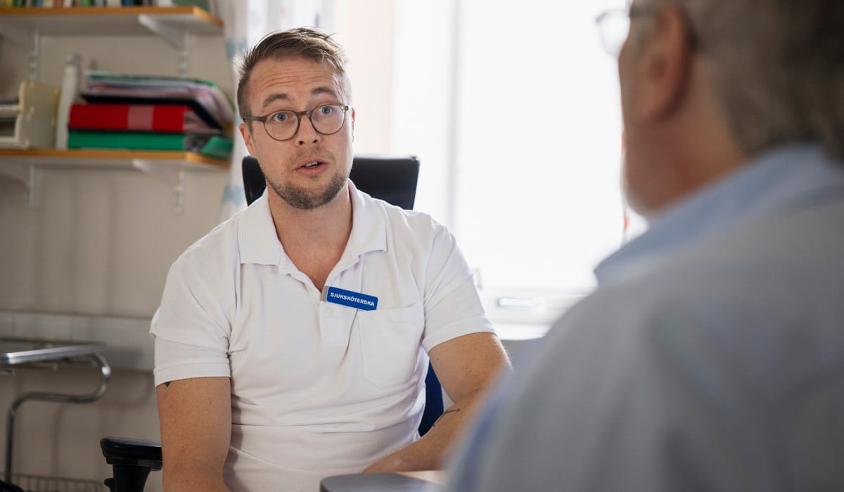 En man sitter i en stol och pratar med en annan man.