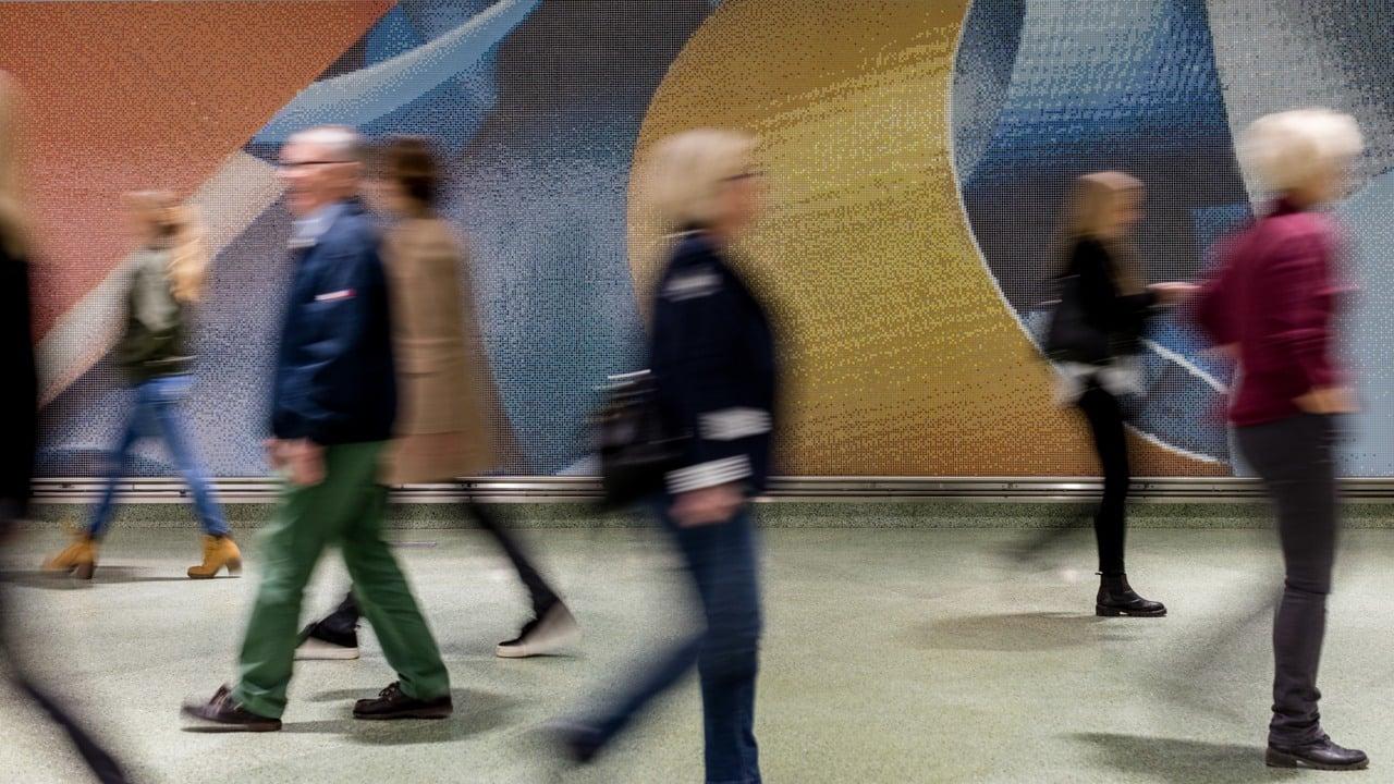 Människor som går i en gångtunnel framför en målad vägg.