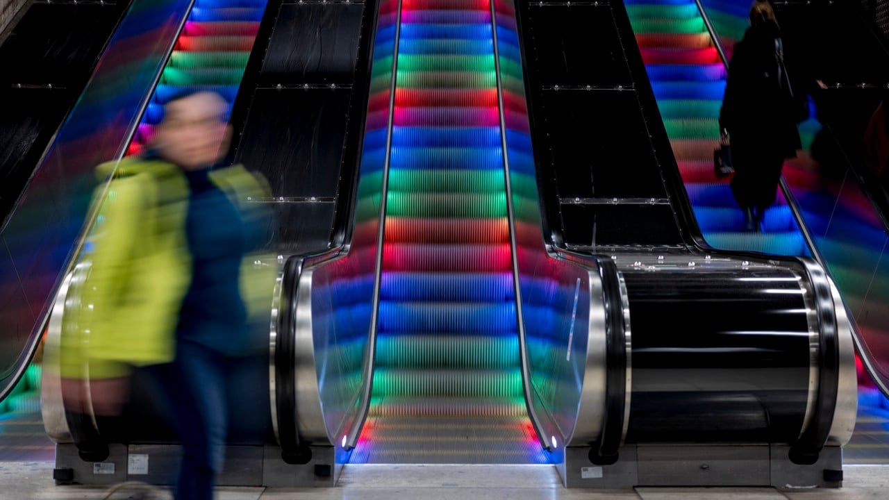 Bild på människor i och vid rulltrappor. Människorna är suddiga eftersom de är i rörelse.