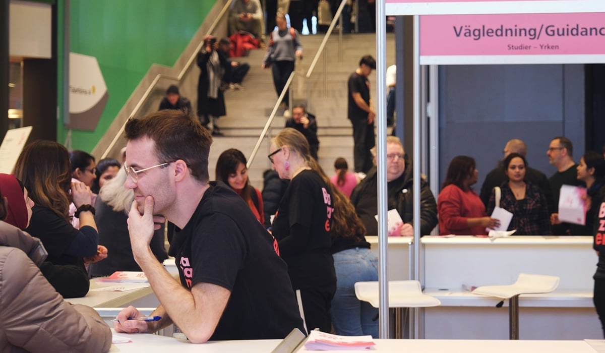 Många människor i bild. En person i förgrunden ger information till annan person över disk.