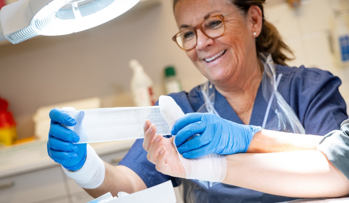 En kvinna i operationskläder lindar bandage om en hand.