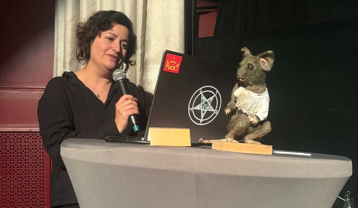 En kvinna står vid ett bord med en bärbar dator och en mikrofon.