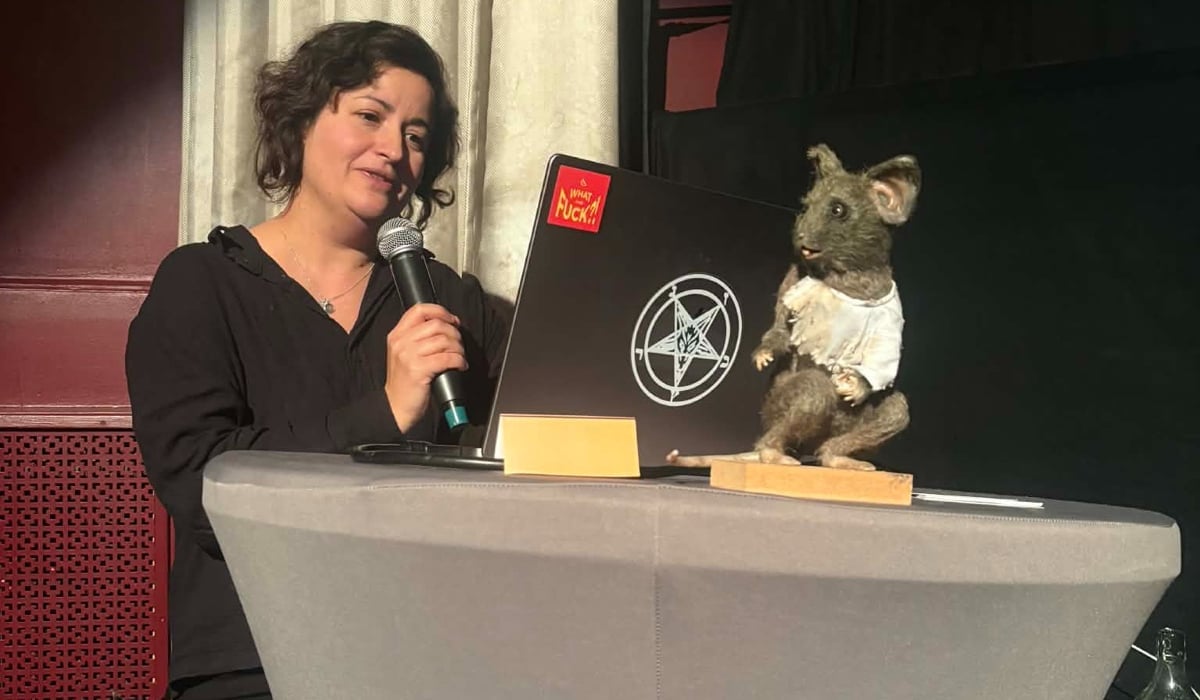 En kvinna står vid ett bord med en bärbar dator och en mikrofon.