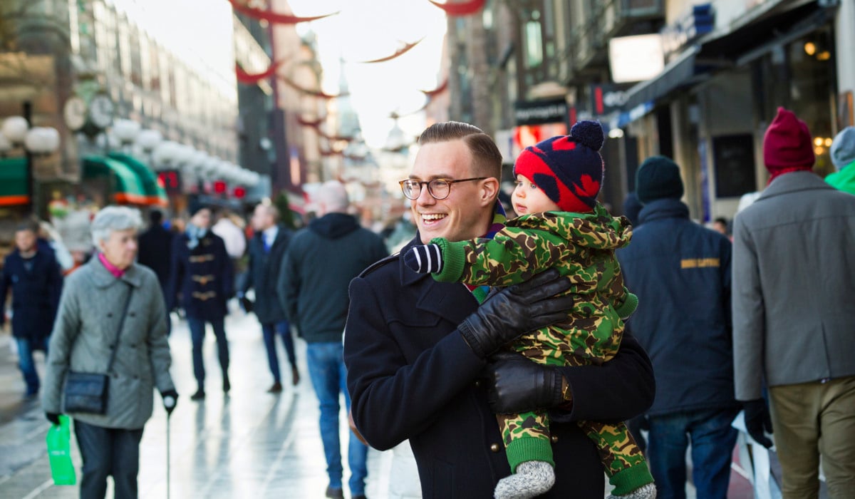 En man håller i ett litet barn på en gata med massor av människor.
