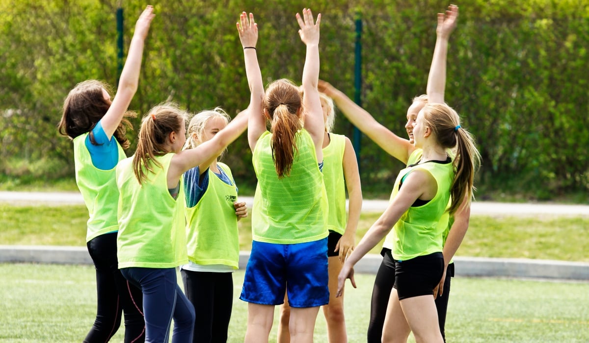 Unga fotbollsspelare i ring utomhus med händerna upp i luften.
